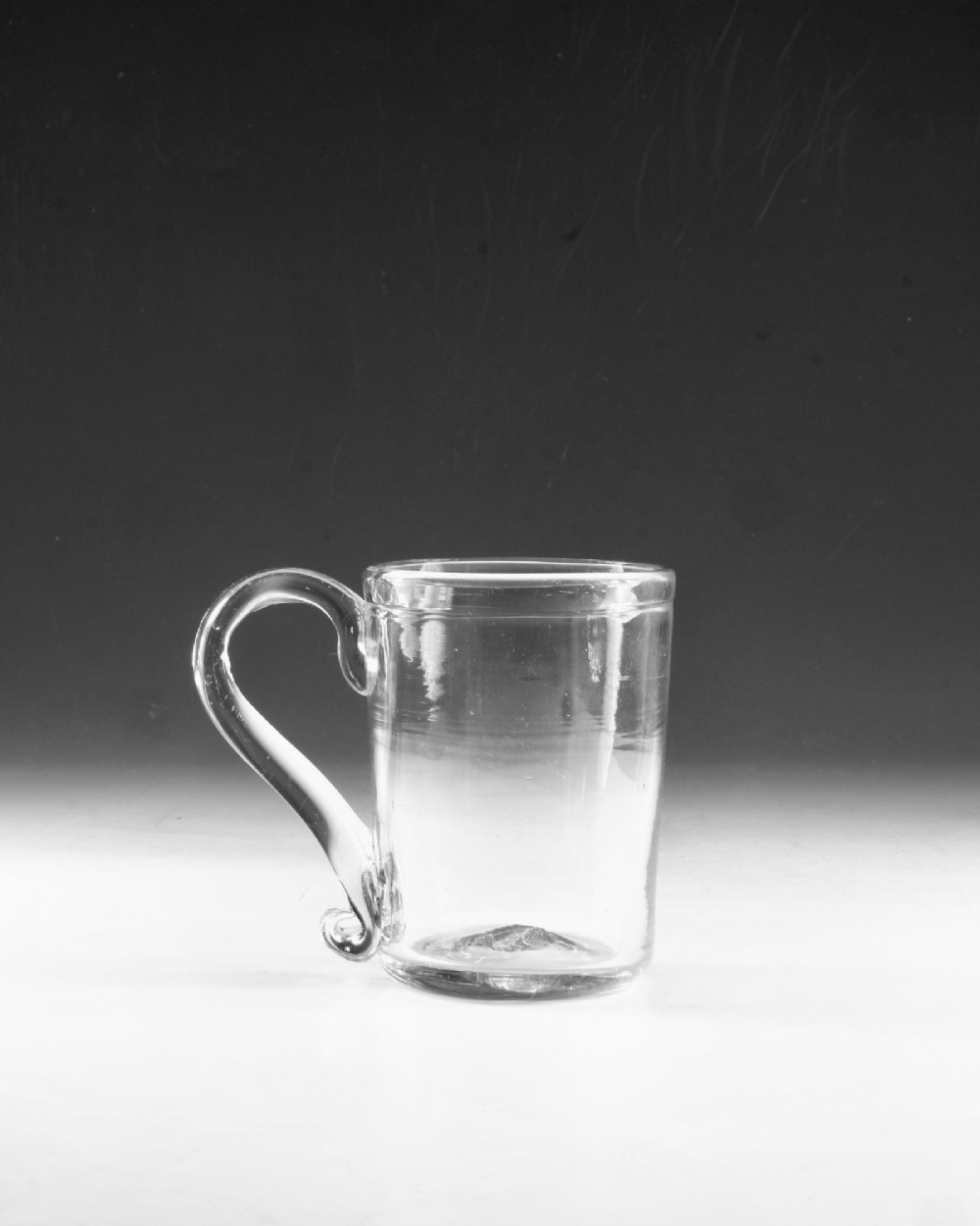 An 18th-century clear glass tankard featuring a cylindrical body and a curved strap handle with a scrolled lower terminal. View III