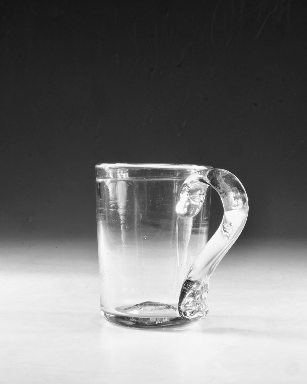 An 18th-century clear glass tankard featuring a cylindrical body and a curved strap handle with a scrolled lower terminal. View IV