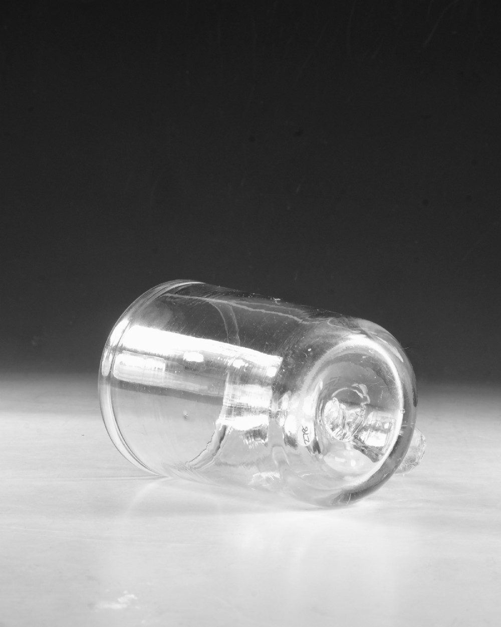 An 18th-century clear glass tankard featuring a cylindrical body and a curved strap handle with a scrolled lower terminal. View V