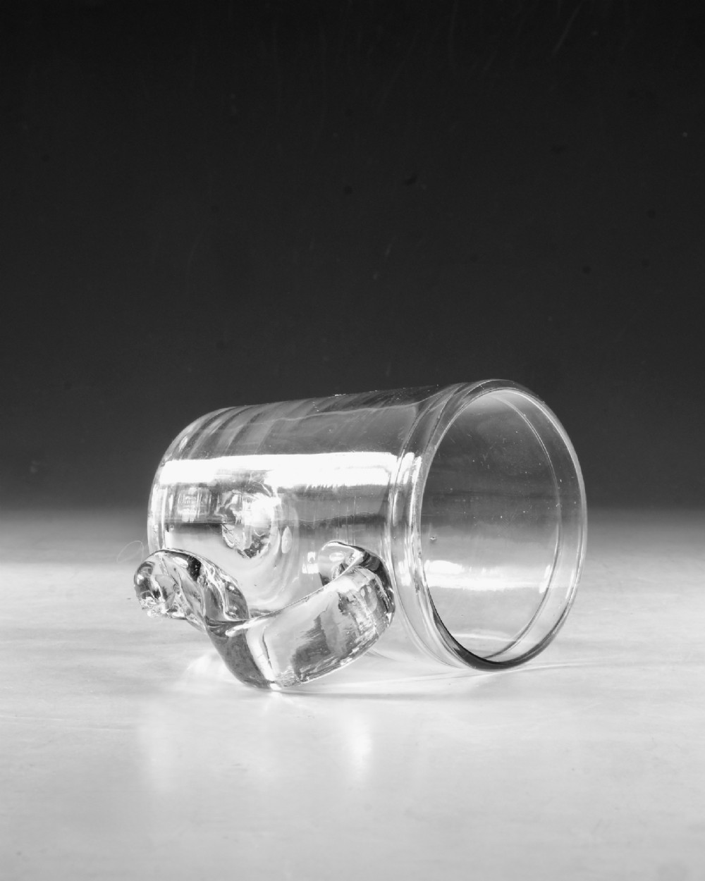 An 18th-century clear glass tankard featuring a cylindrical body and a curved strap handle with a scrolled lower terminal. View VI