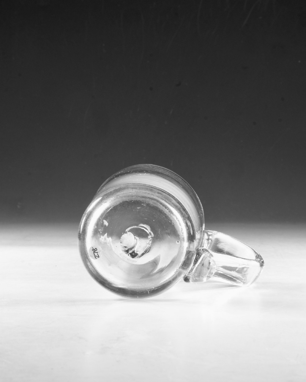 An 18th-century clear glass tankard featuring a cylindrical body and a curved strap handle with a scrolled lower terminal. View VII