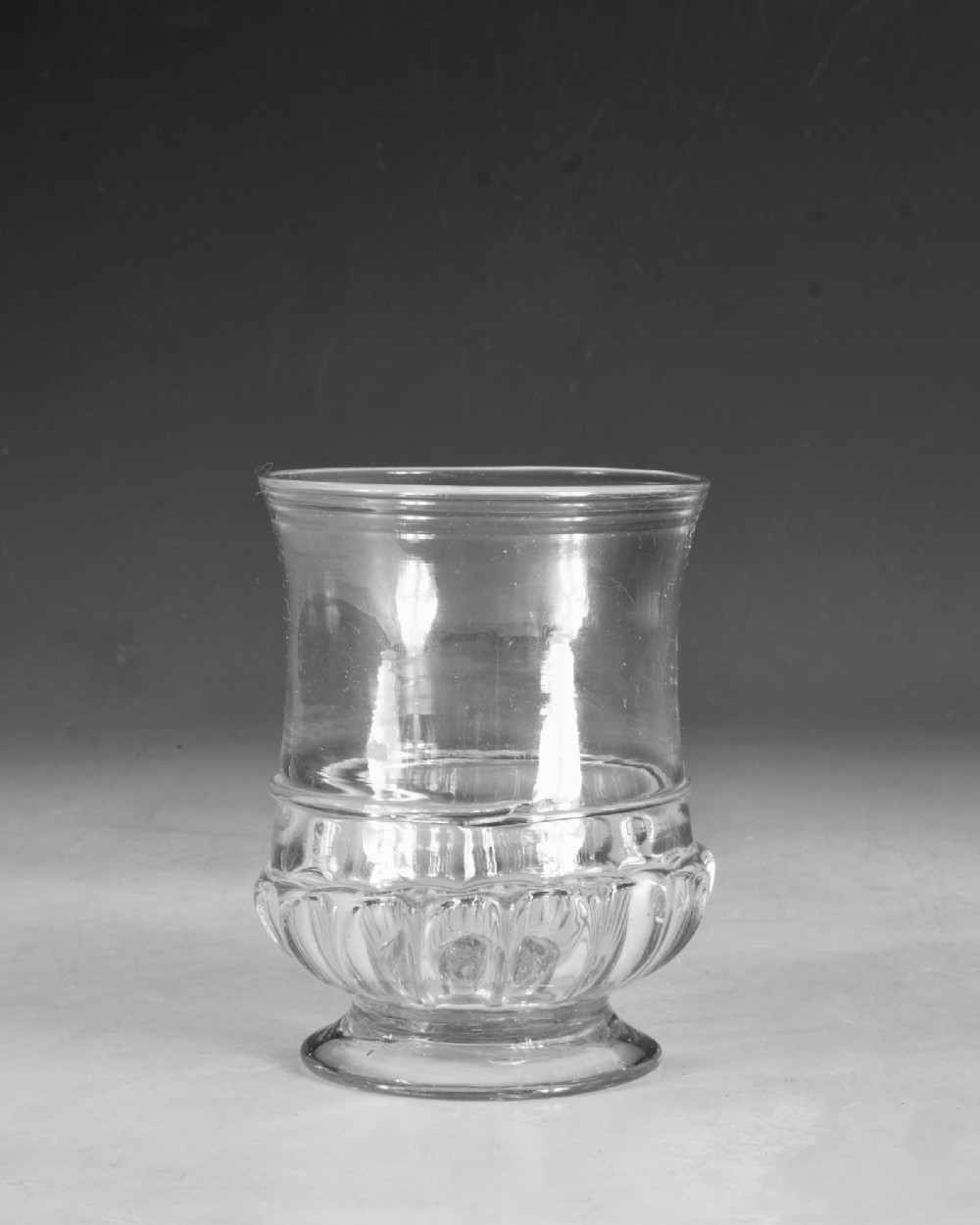 A clear 18th-century Georgian glass drinking vessel featuring a flared rim, a ribbed lower body, and a low circular pedestal base. View II