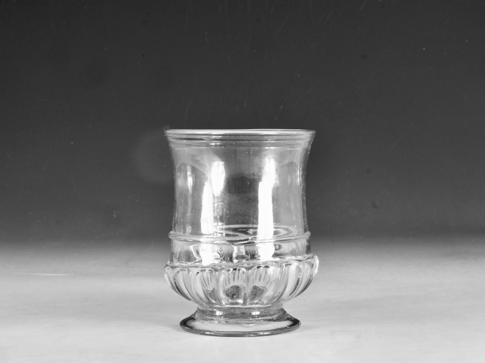 A clear 18th-century Georgian glass drinking vessel featuring a flared rim, a ribbed lower body, and a low circular pedestal base. View VI