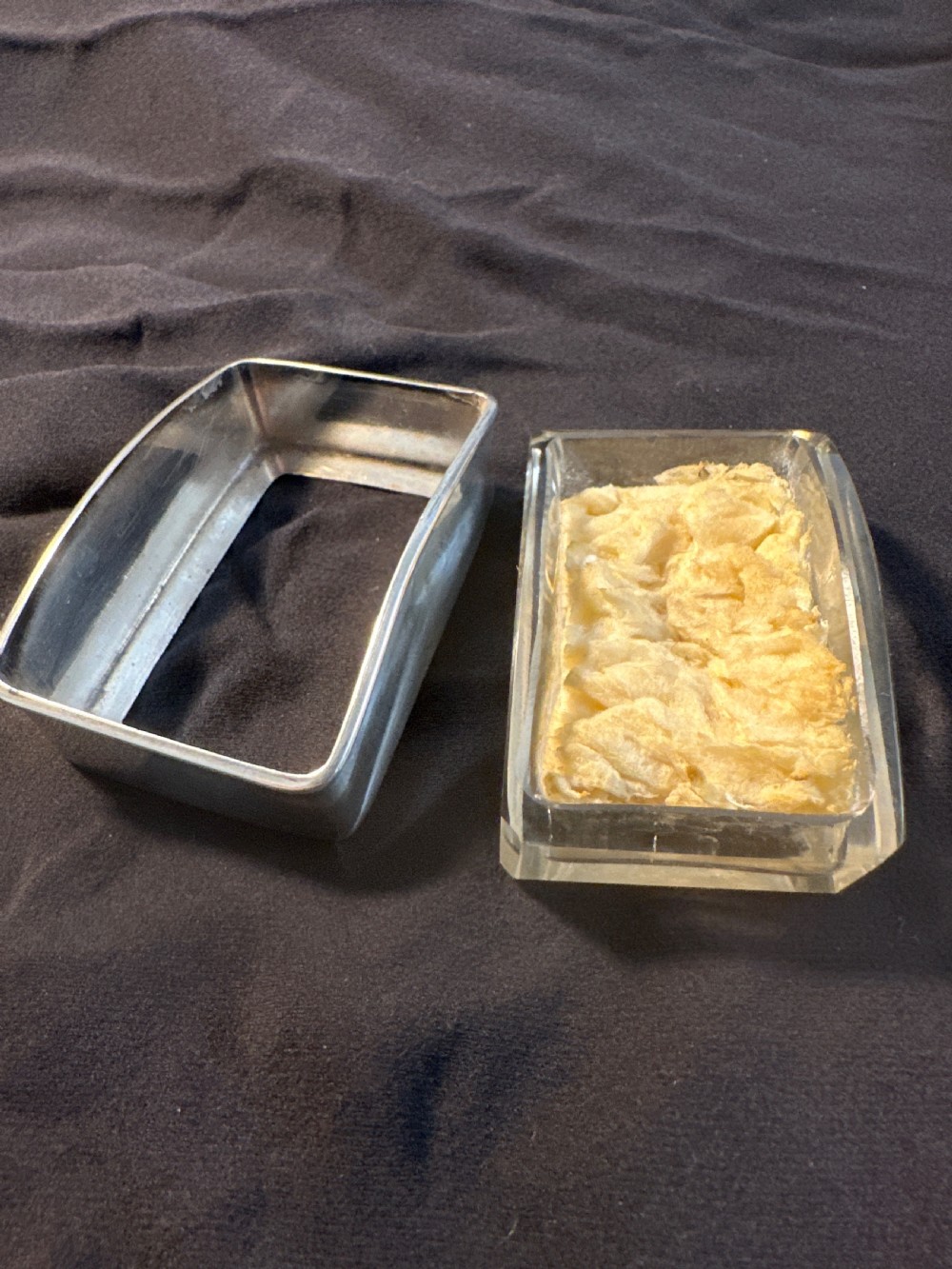 A rectangular silver vessel with a curved rim containing a light yellow natural sponge. View II