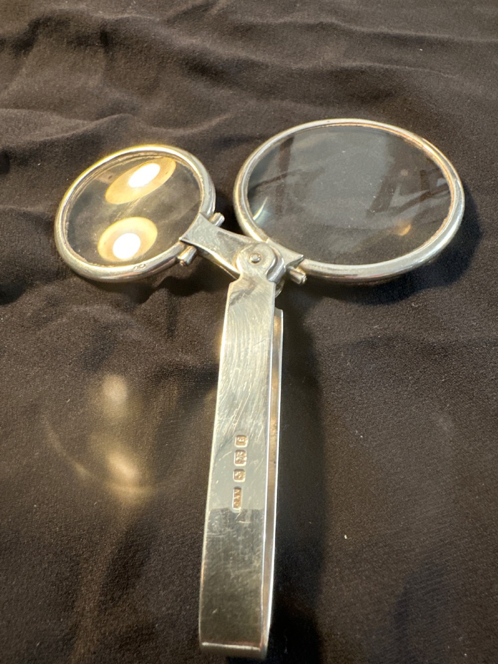 An Edwardian hallmarked sterling silver folding double-lens magnifying glass with two circular lenses attached to a hinged handle.