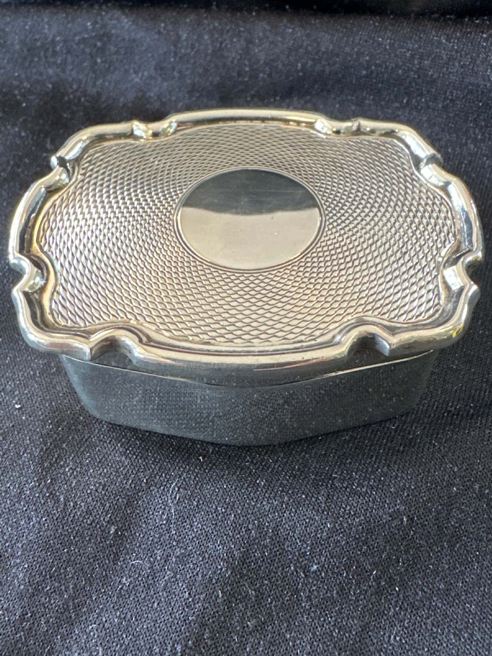An Edwardian sterling silver shaped box with engine-turned geometric detailing on the lid and a central plain circular cartouche.
