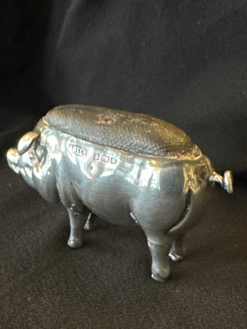 An Edwardian sterling silver pin cushion modelled in the shape of a standing pig with a fabric insert and visible hallmarked stamps on its side. View V