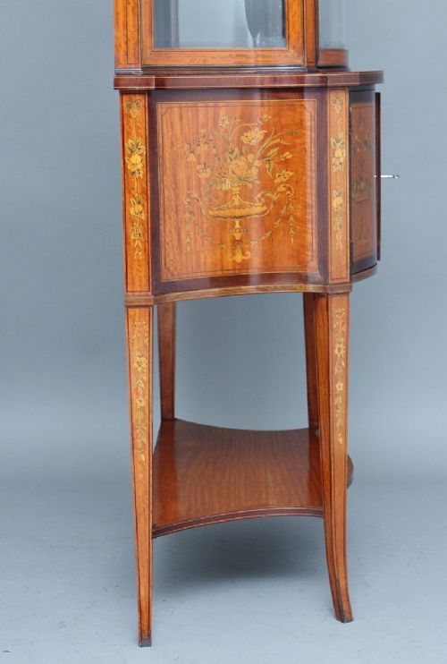 A 19th-century satinwood display cabinet featuring a swan-neck pediment, curved central glass door, and marquetry inlaid lower doors on square tapered legs. View VI
