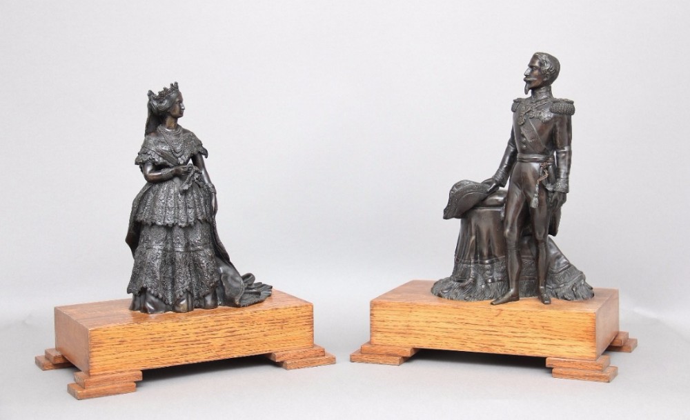 A pair of 19th-century dark bronze figures depicting a gentleman in military uniform and a lady in formal dress, mounted on stepped wooden bases.