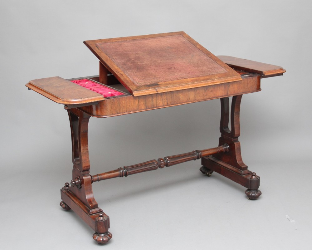 A 19th-century rosewood writing table featuring an adjustable leather-inset slope, side compartments, and a turned stretcher supported by carved trestle legs.