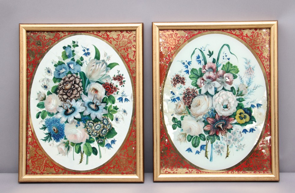 A pair of early 19th-century framed botanical paintings depicting colourful floral bouquets within oval apertures surrounded by red and gold patterned borders.