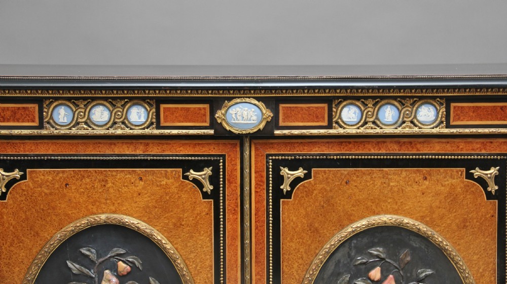 A 19th-century ebonised and amboyna wood credenza featuring central doors with oval pietre dure panels, porcelain medallion inserts, gilt bronze mounts, and curved glass side compartments. View XV