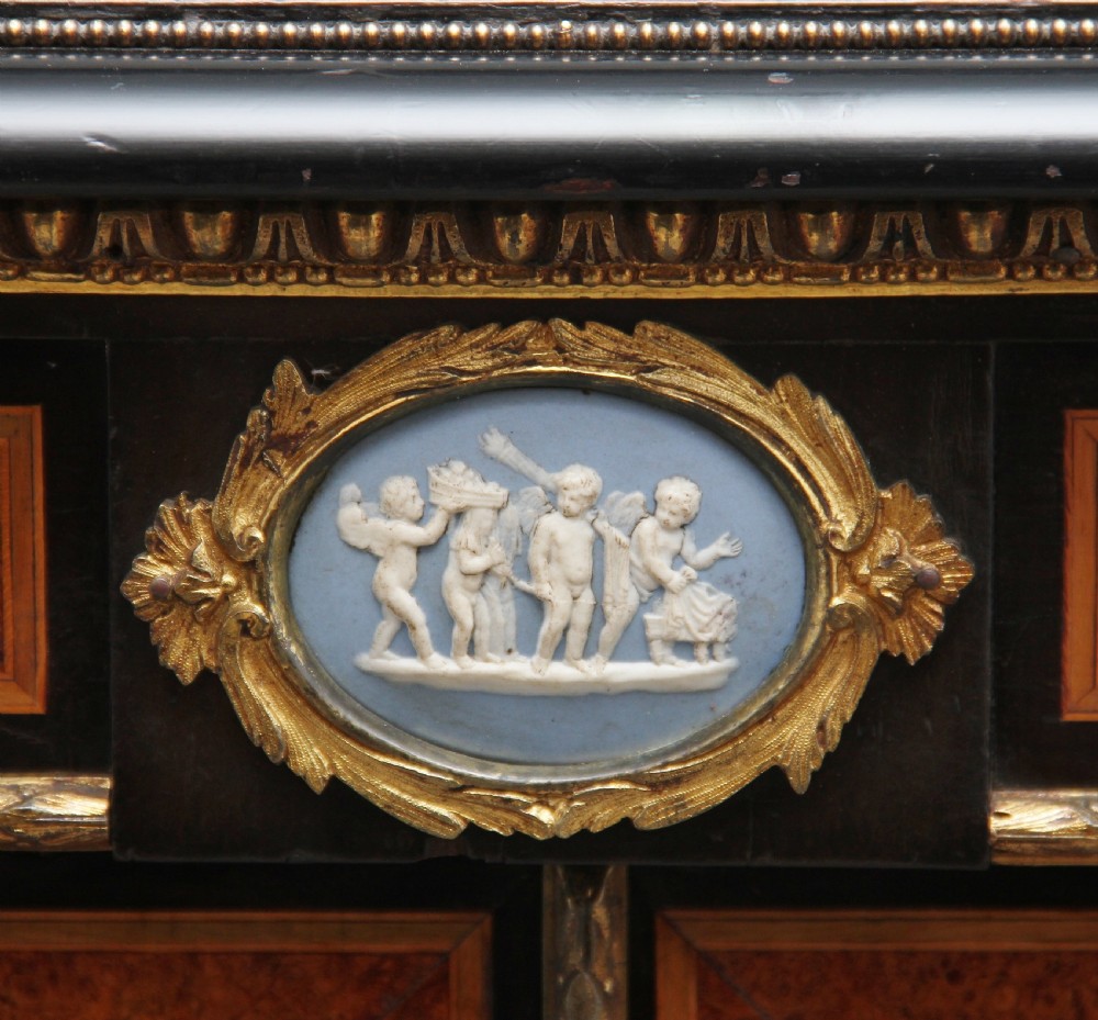 A 19th-century ebonised and amboyna wood credenza featuring central doors with oval pietre dure panels, porcelain medallion inserts, gilt bronze mounts, and curved glass side compartments. View XVII