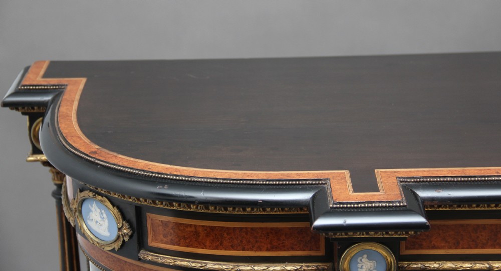 A 19th-century ebonised and amboyna wood credenza featuring central doors with oval pietre dure panels, porcelain medallion inserts, gilt bronze mounts, and curved glass side compartments. View XIX