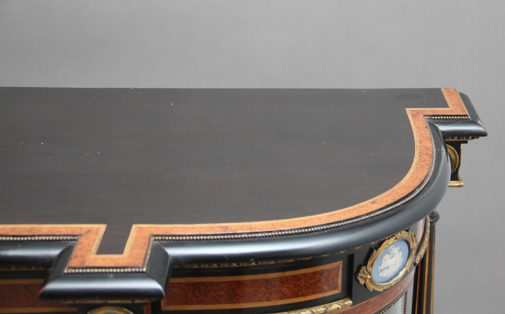 A 19th-century ebonised and amboyna wood credenza featuring central doors with oval pietre dure panels, porcelain medallion inserts, gilt bronze mounts, and curved glass side compartments. View XX