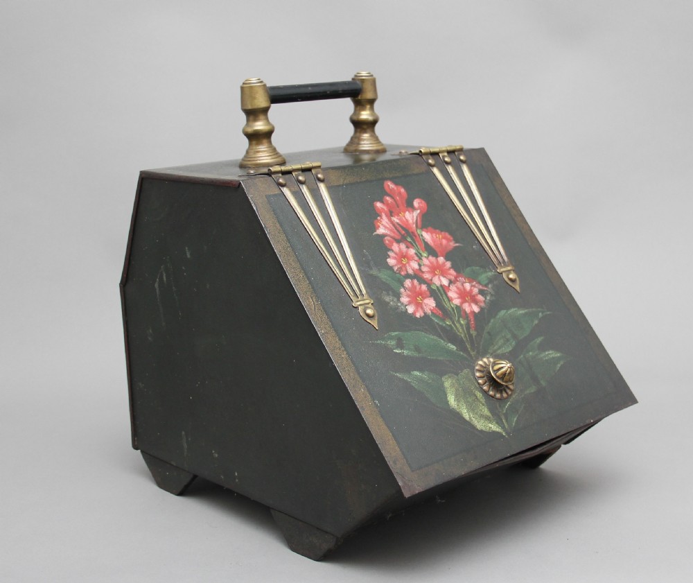 A nineteenth-century black metal coal box featuring a slanted drop front decorated with hand-painted pink flowers, brass strap hinges, a brass knob, and a top carrying handle.