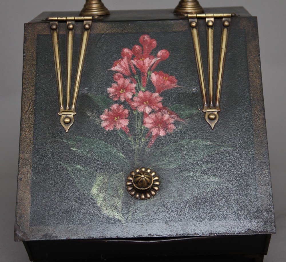 A nineteenth-century black metal coal box featuring a slanted drop front decorated with hand-painted pink flowers, brass strap hinges, a brass knob, and a top carrying handle. View VI