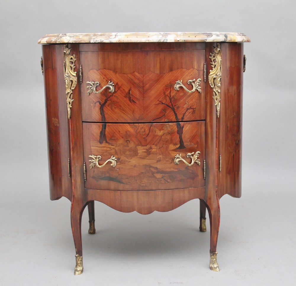 An early 19th-century French marquetry cabinet with a curved front, marble top, detailed wood inlay depicting a scenic landscape, and ornamental brass mounts.