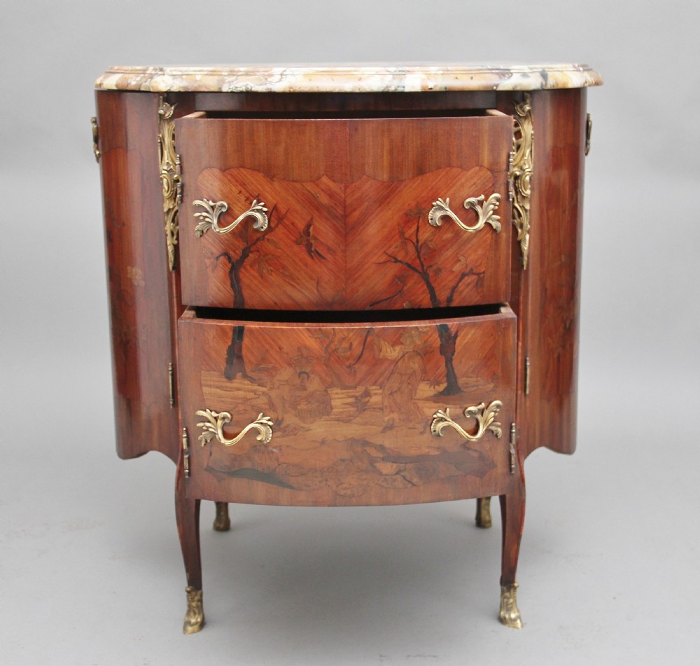 An early 19th-century French marquetry cabinet with a curved front, marble top, detailed wood inlay depicting a scenic landscape, and ornamental brass mounts. View II
