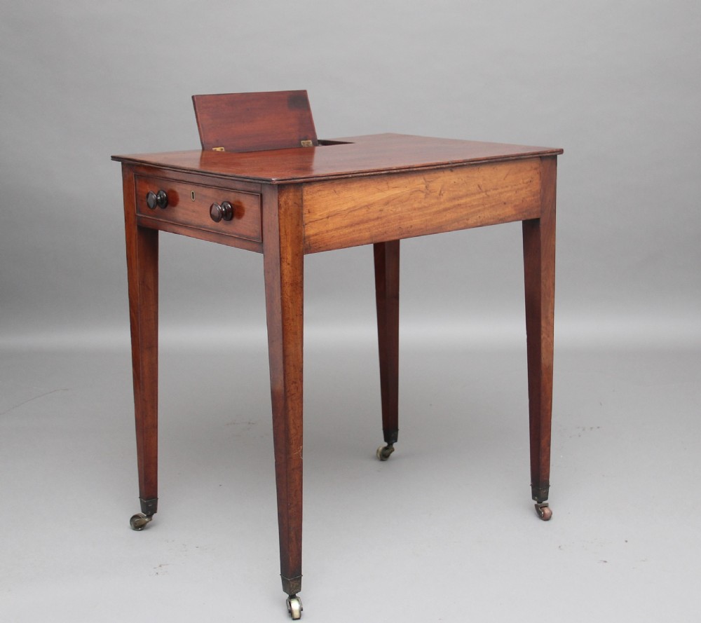 An early nineteenth-century mahogany writing table featuring square tapered legs on brass castors, a single drawer with turned wooden handles, and an adjustable reading slope set into the top.