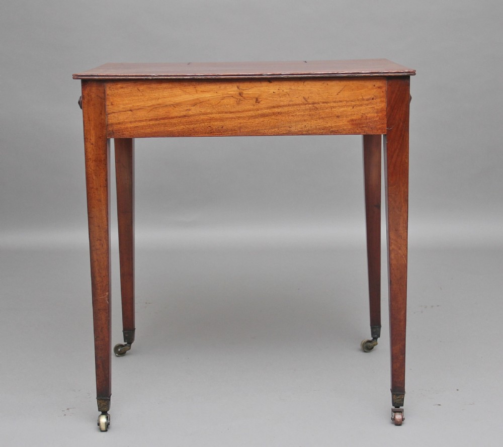 An early nineteenth-century mahogany writing table featuring square tapered legs on brass castors, a single drawer with turned wooden handles, and an adjustable reading slope set into the top. View II
