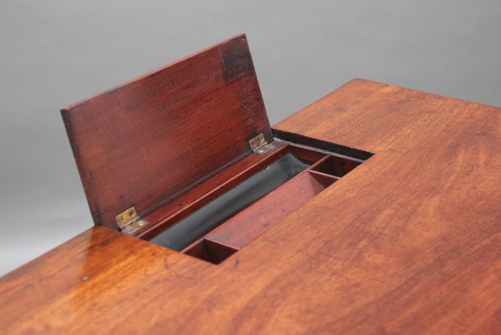 An early nineteenth-century mahogany writing table featuring square tapered legs on brass castors, a single drawer with turned wooden handles, and an adjustable reading slope set into the top. View IV