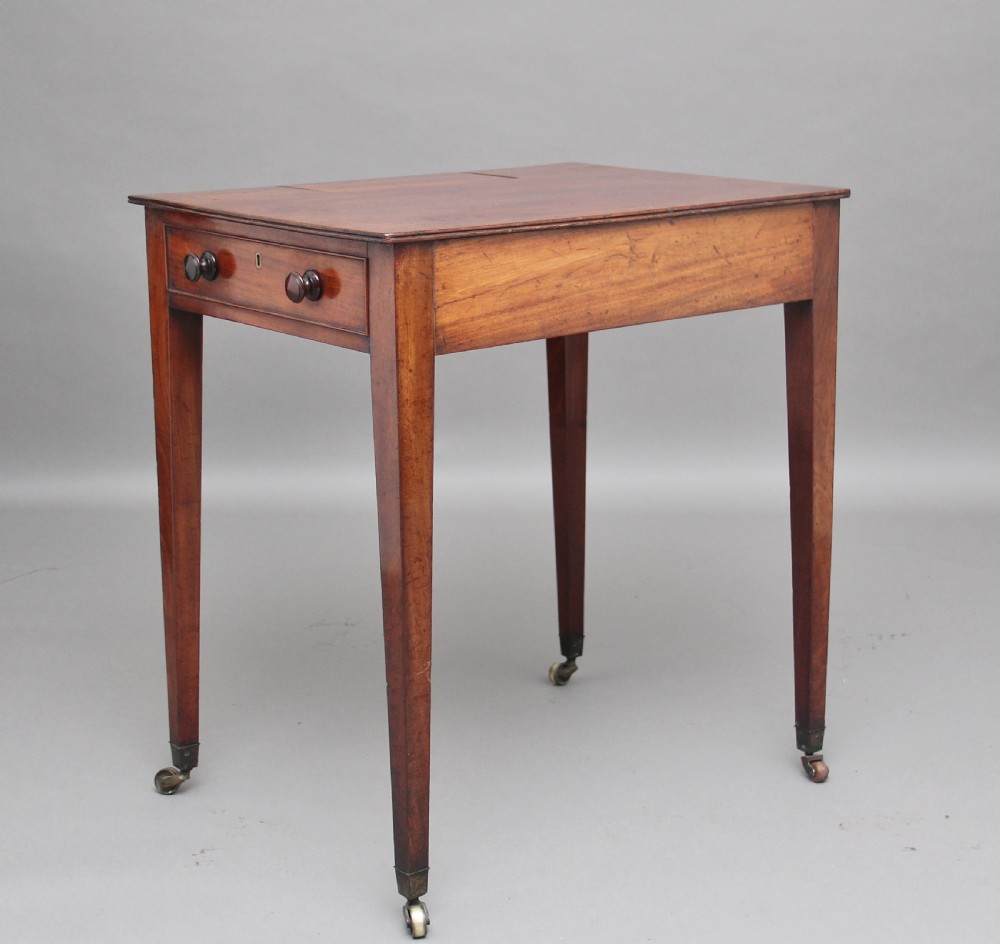 An early nineteenth-century mahogany writing table featuring square tapered legs on brass castors, a single drawer with turned wooden handles, and an adjustable reading slope set into the top. View V