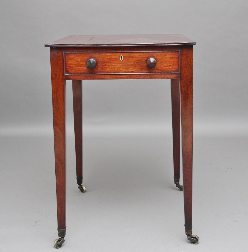 An early nineteenth-century mahogany writing table featuring square tapered legs on brass castors, a single drawer with turned wooden handles, and an adjustable reading slope set into the top. View VI