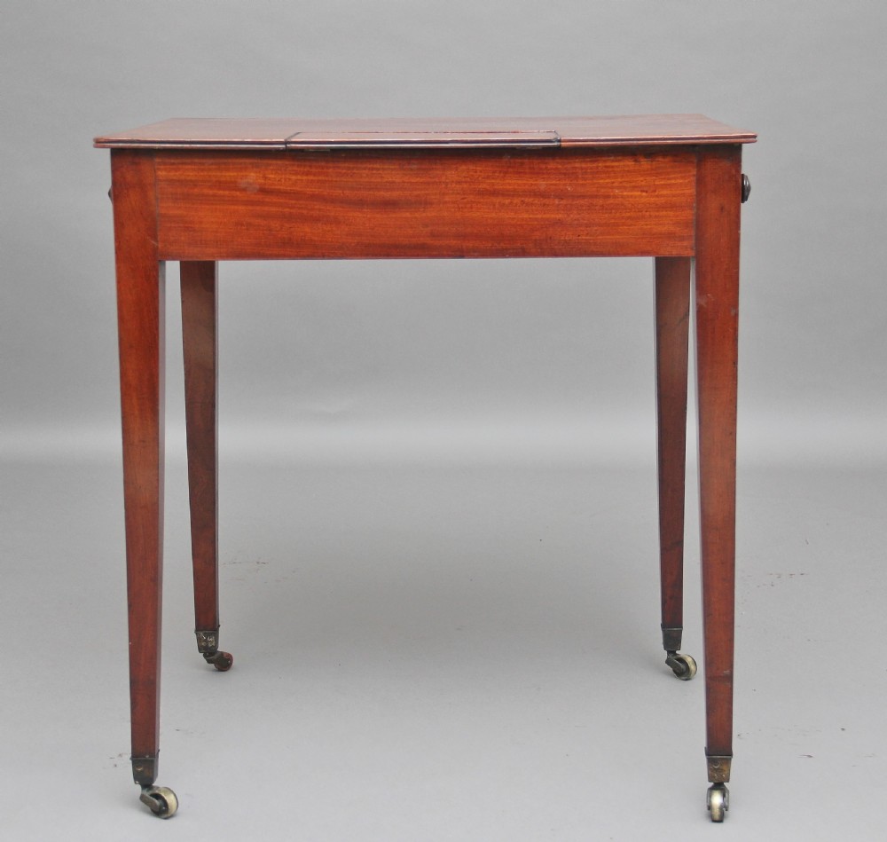 An early nineteenth-century mahogany writing table featuring square tapered legs on brass castors, a single drawer with turned wooden handles, and an adjustable reading slope set into the top. View VII