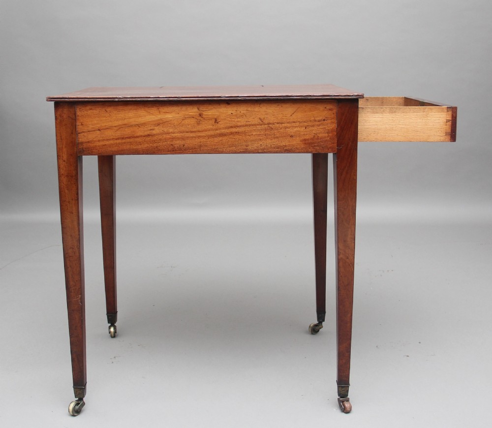 An early nineteenth-century mahogany writing table featuring square tapered legs on brass castors, a single drawer with turned wooden handles, and an adjustable reading slope set into the top. View IX