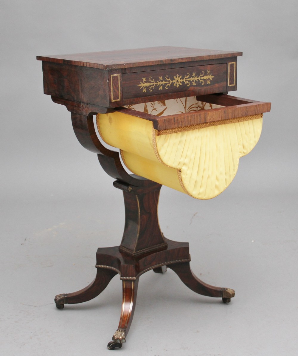 An early 19th-century dark rosewood sewing table featuring brass marquetry inlay on the drawer front, a yellow pleated fabric work basket, and a pedestal base on quadform sabre legs with brass feet. View II