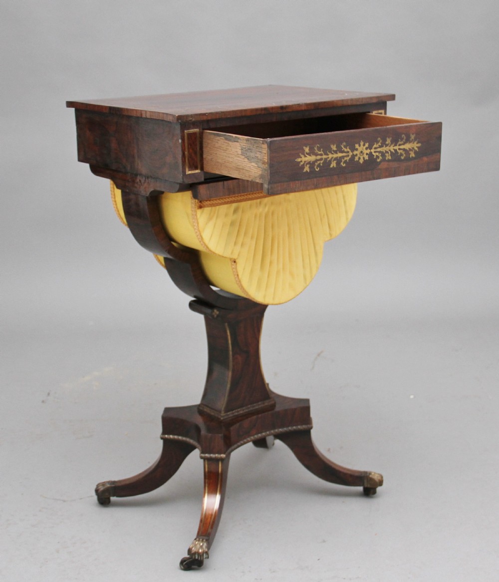 An early 19th-century dark rosewood sewing table featuring brass marquetry inlay on the drawer front, a yellow pleated fabric work basket, and a pedestal base on quadform sabre legs with brass feet. View III