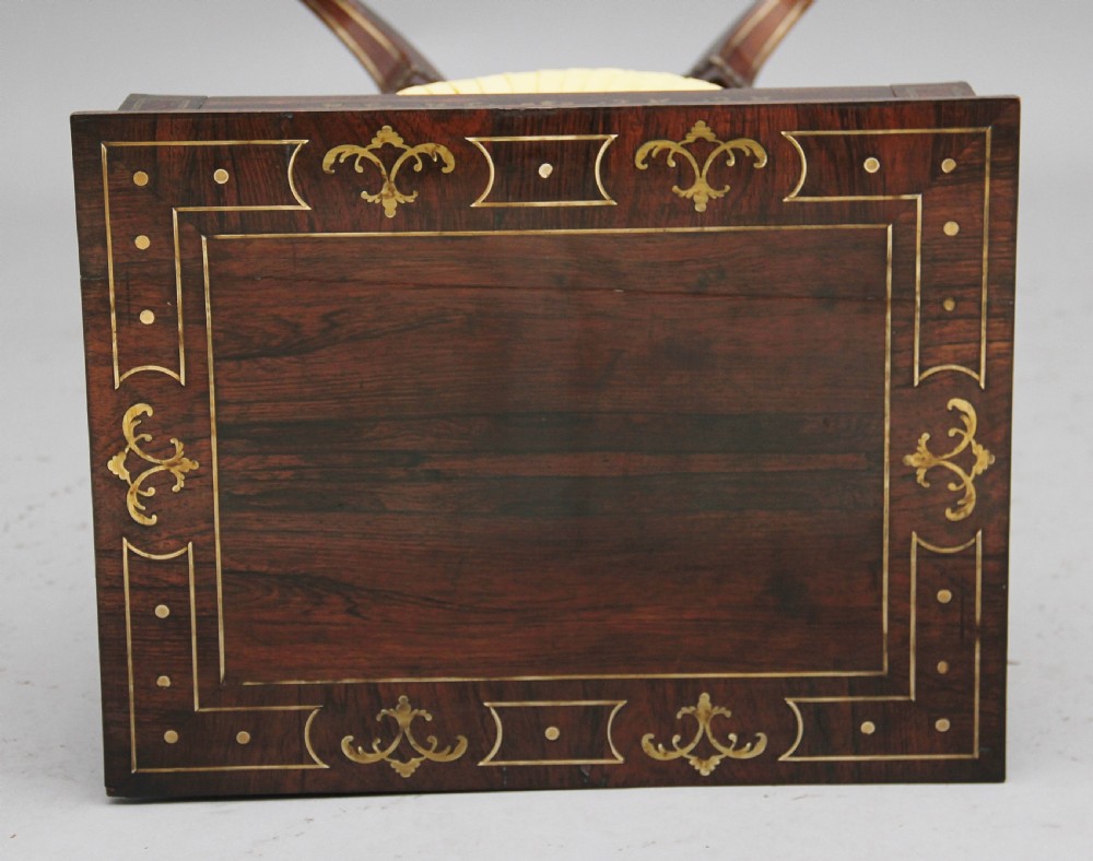 An early 19th-century dark rosewood sewing table featuring brass marquetry inlay on the drawer front, a yellow pleated fabric work basket, and a pedestal base on quadform sabre legs with brass feet. View IX