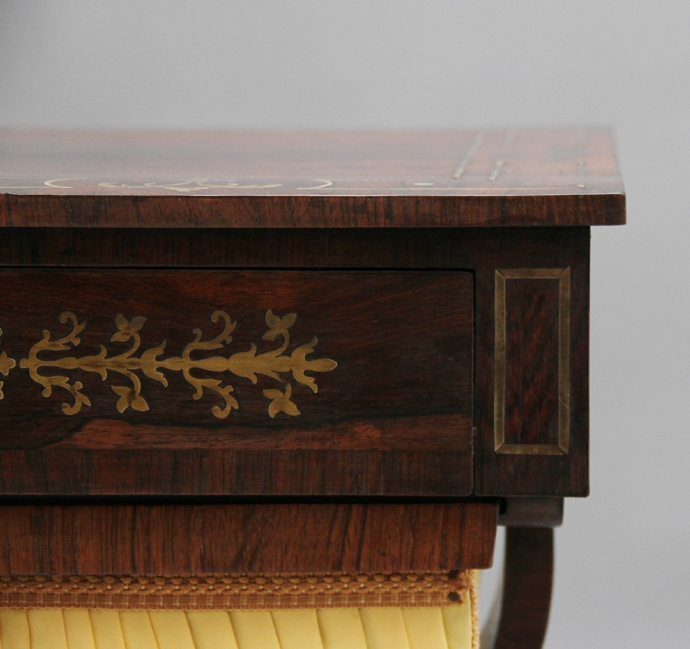 An early 19th-century dark rosewood sewing table featuring brass marquetry inlay on the drawer front, a yellow pleated fabric work basket, and a pedestal base on quadform sabre legs with brass feet. View XI