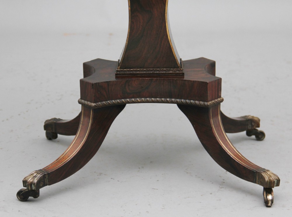 An early 19th-century dark rosewood sewing table featuring brass marquetry inlay on the drawer front, a yellow pleated fabric work basket, and a pedestal base on quadform sabre legs with brass feet. View XII
