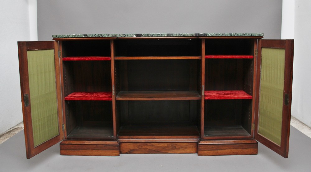 An early nineteenth-century rosewood breakfront cabinet featuring a green marble top, open central shelving section, and flanking doors with pleated fabric panels on a solid plinth base. View II