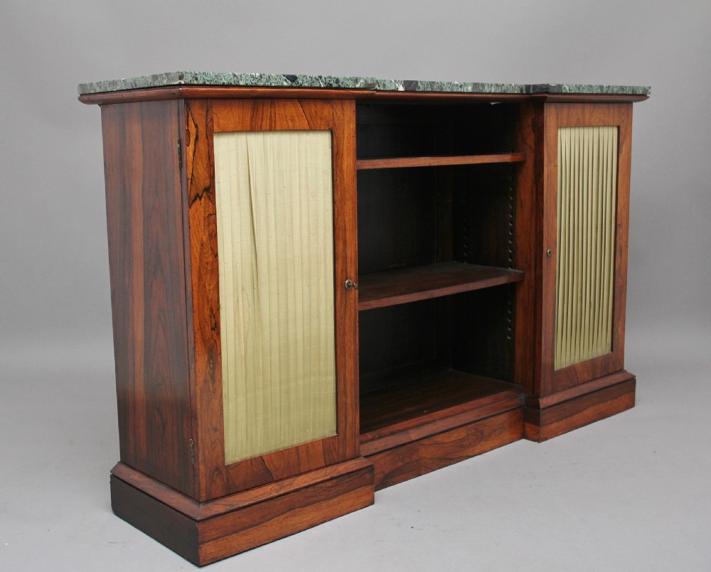 An early nineteenth-century rosewood breakfront cabinet featuring a green marble top, open central shelving section, and flanking doors with pleated fabric panels on a solid plinth base. View III
