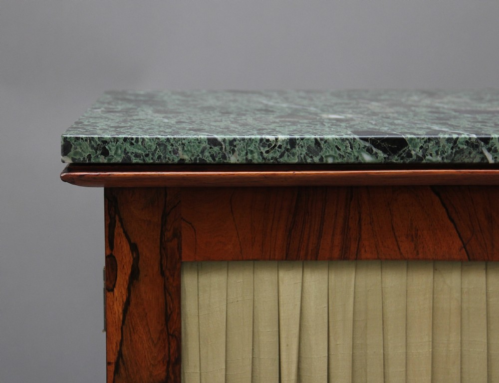 An early nineteenth-century rosewood breakfront cabinet featuring a green marble top, open central shelving section, and flanking doors with pleated fabric panels on a solid plinth base. View V