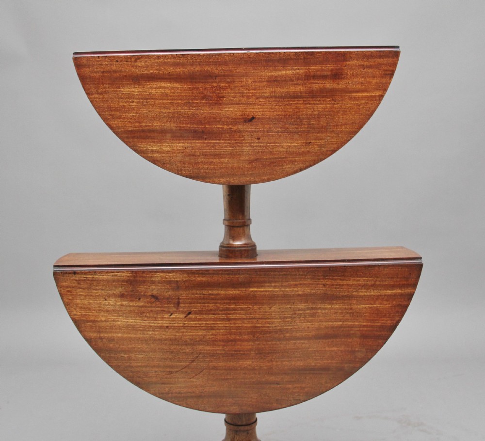 An early nineteenth-century mahogany two-tier dumbwaiter featuring circular drop-leaf surfaces, a turned central column support, and reeded tripod legs with brass castors. View X