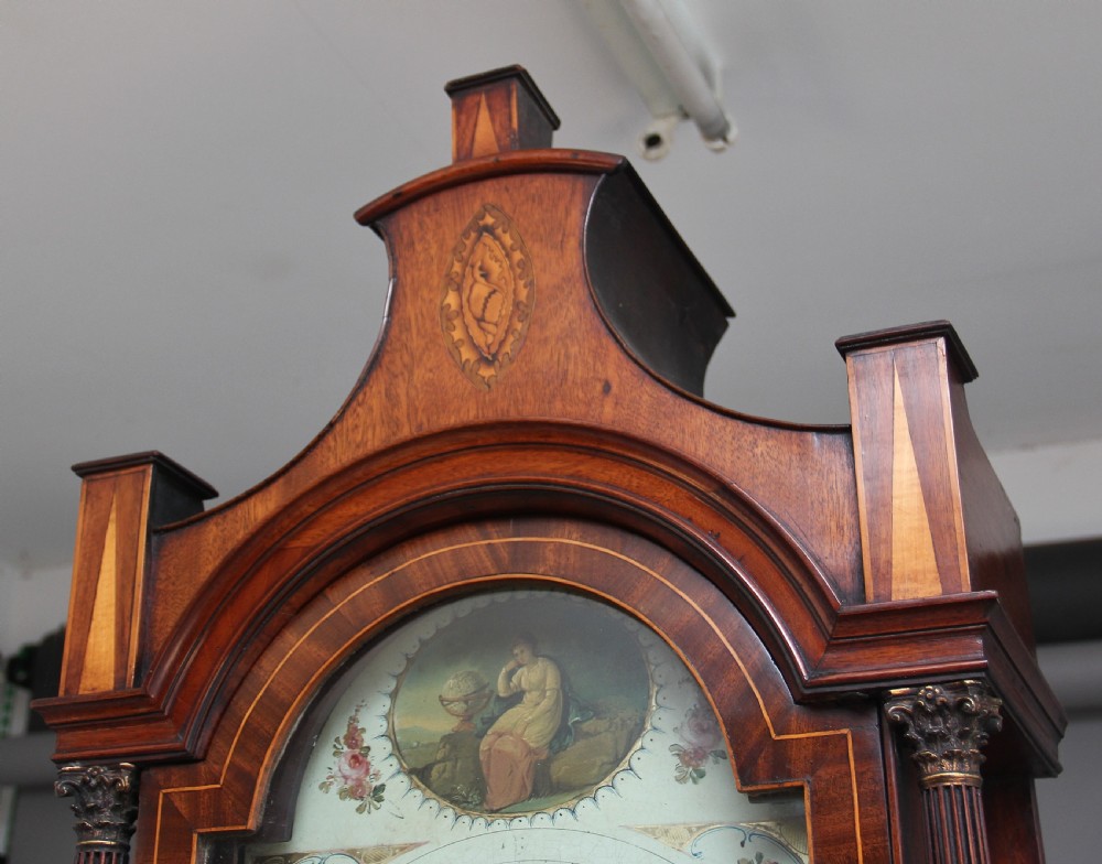 A 19th-century mahogany longcase clock featuring a swan-neck pediment hood, an arched painted clock dial, a flame mahogany trunk door with marquetry inlay, and a plinth base. View IX