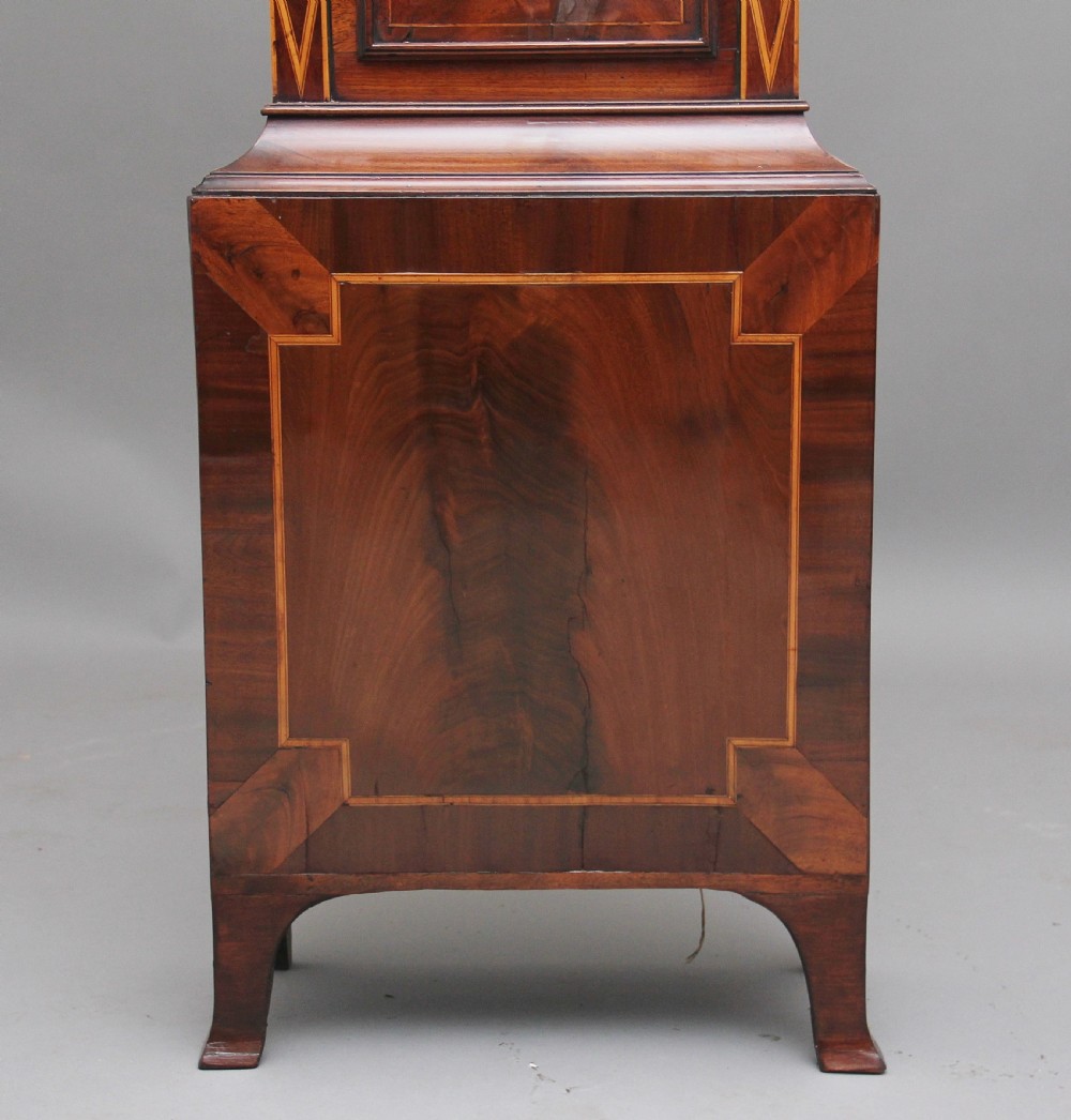 A 19th-century mahogany longcase clock featuring a swan-neck pediment hood, an arched painted clock dial, a flame mahogany trunk door with marquetry inlay, and a plinth base. View XV