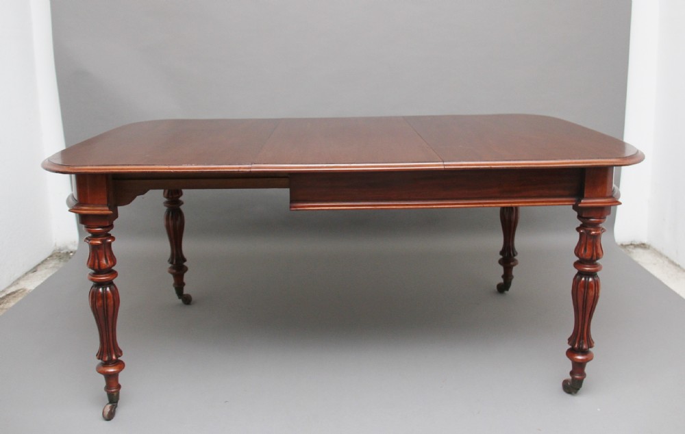 A 19th-century mahogany extending dining table with rounded corners, a polished rectangular top, turned legs, and brass castors.