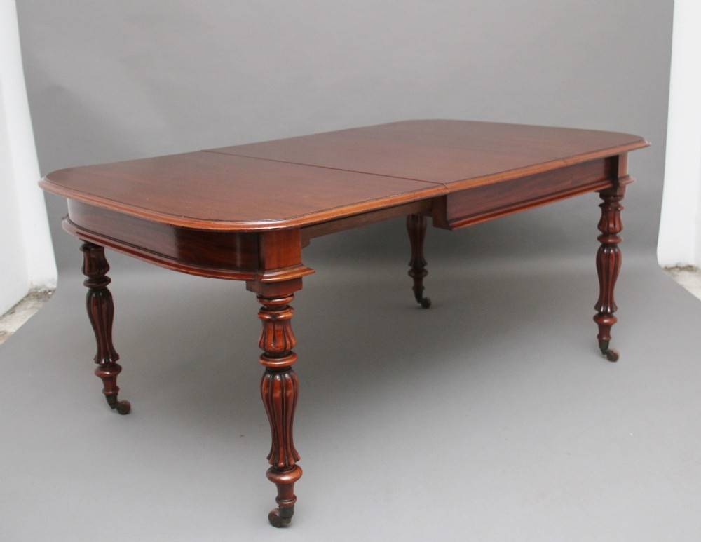 A 19th-century mahogany extending dining table with rounded corners, a polished rectangular top, turned legs, and brass castors. View II