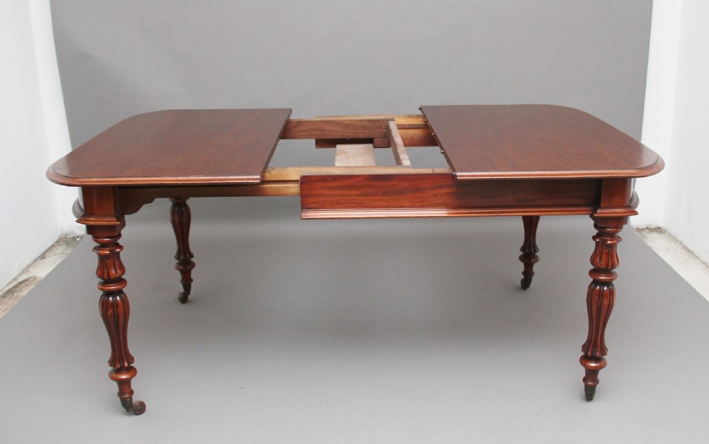 A 19th-century mahogany extending dining table with rounded corners, a polished rectangular top, turned legs, and brass castors. View IV