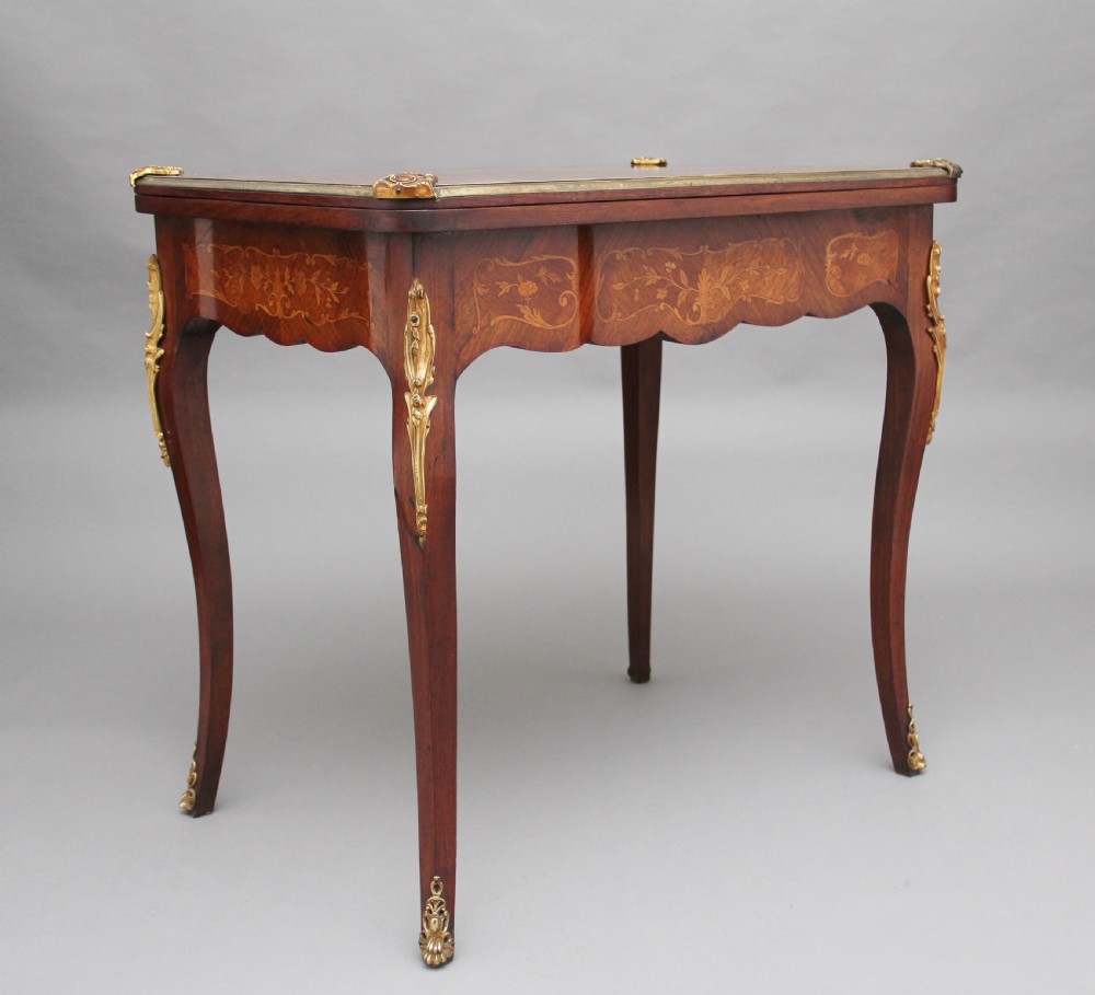 A 19th-century French Rococo revival kingwood fold-over card table with floral marquetry inlay, cabriole legs, and ornate gilt ormolu mounts.