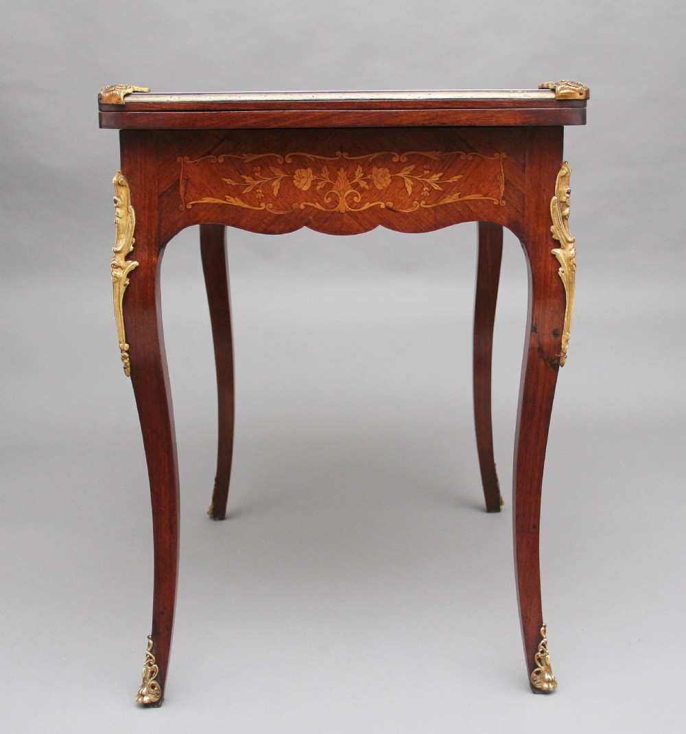 A 19th-century French Rococo revival kingwood fold-over card table with floral marquetry inlay, cabriole legs, and ornate gilt ormolu mounts. View X