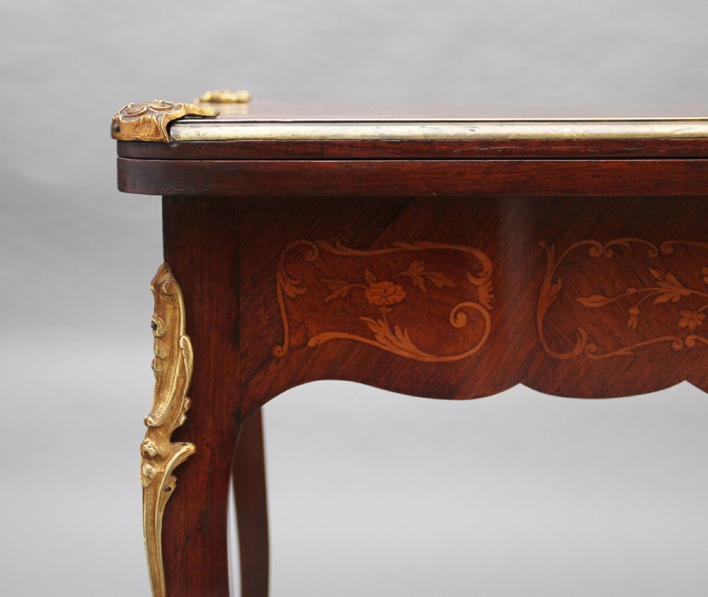 A 19th-century French Rococo revival kingwood fold-over card table with floral marquetry inlay, cabriole legs, and ornate gilt ormolu mounts. View XV