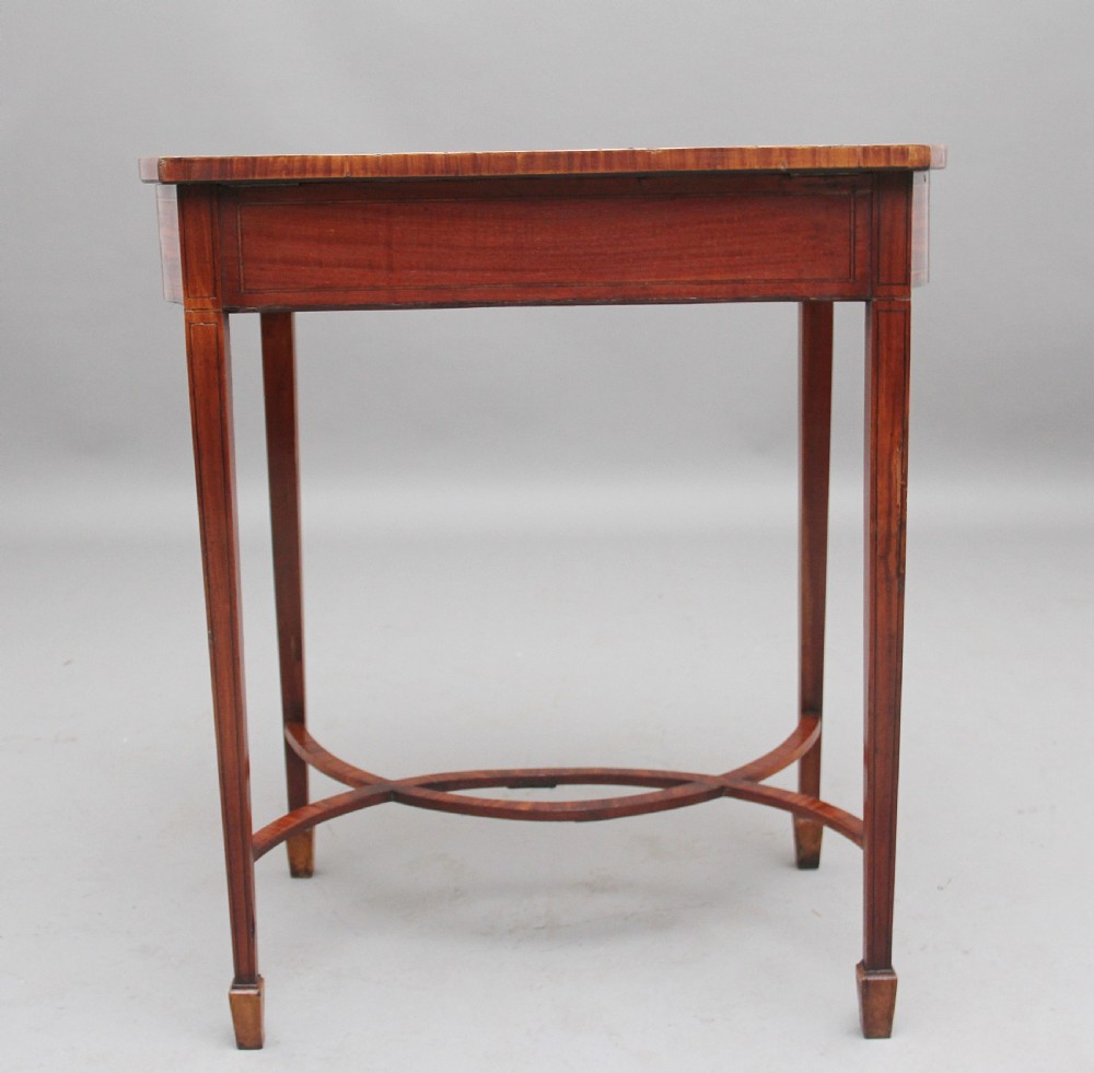 An Edwardian inlaid satinwood bijouterie table featuring a glazed rectangular top, curved side profile, tapered square legs, and curved cross-stretchers. View VIII