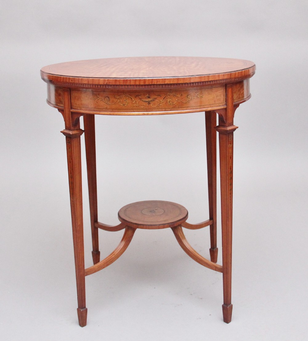 An oval 19th-century satinwood occasional table featuring floral marquetry along the apron, tapered square legs, and a small circular undertier.