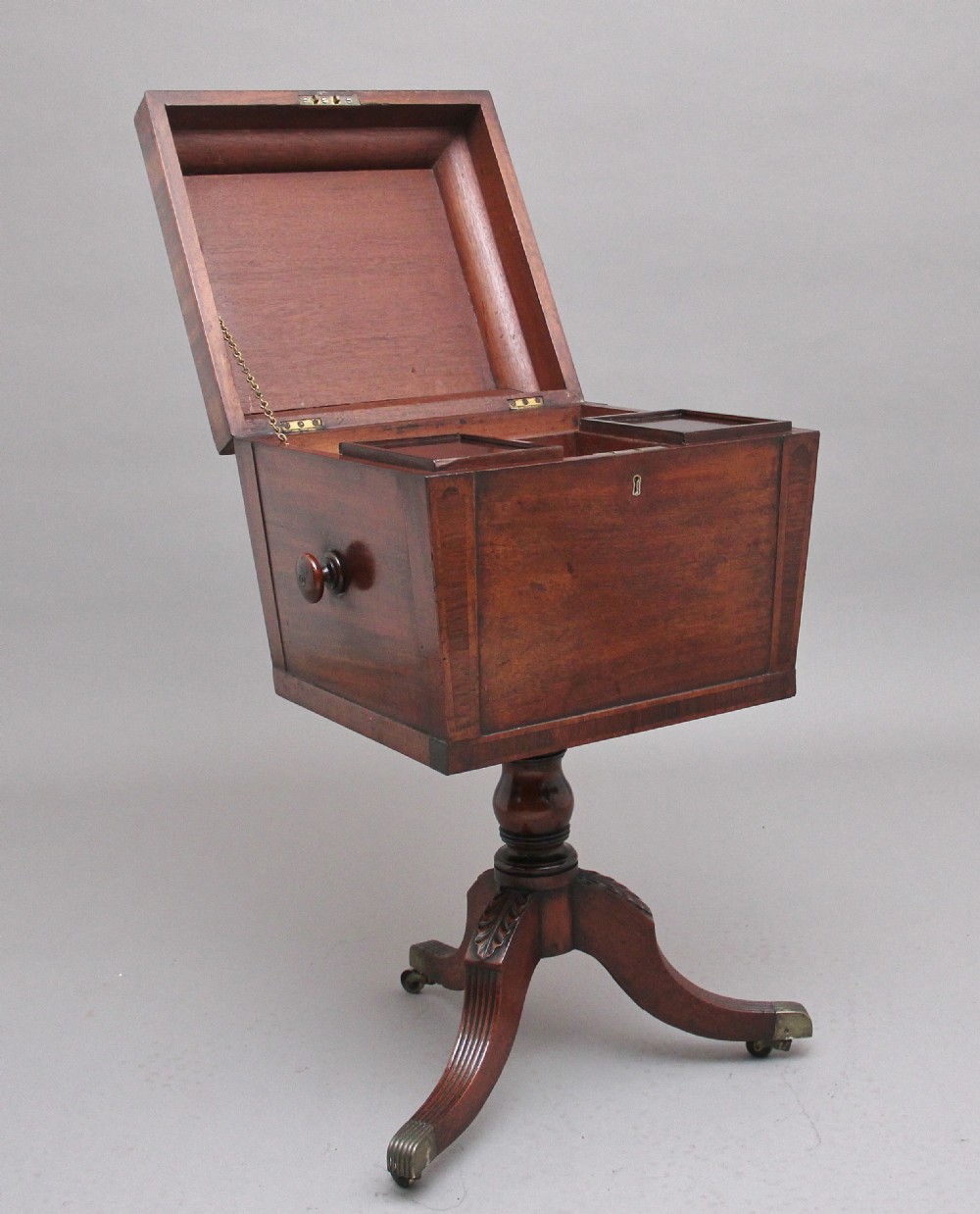 An early 19th-century Regency mahogany teapoy with a hinged tapered box mounted on a turned pedestal and reeded tripod legs with brass castors. View II